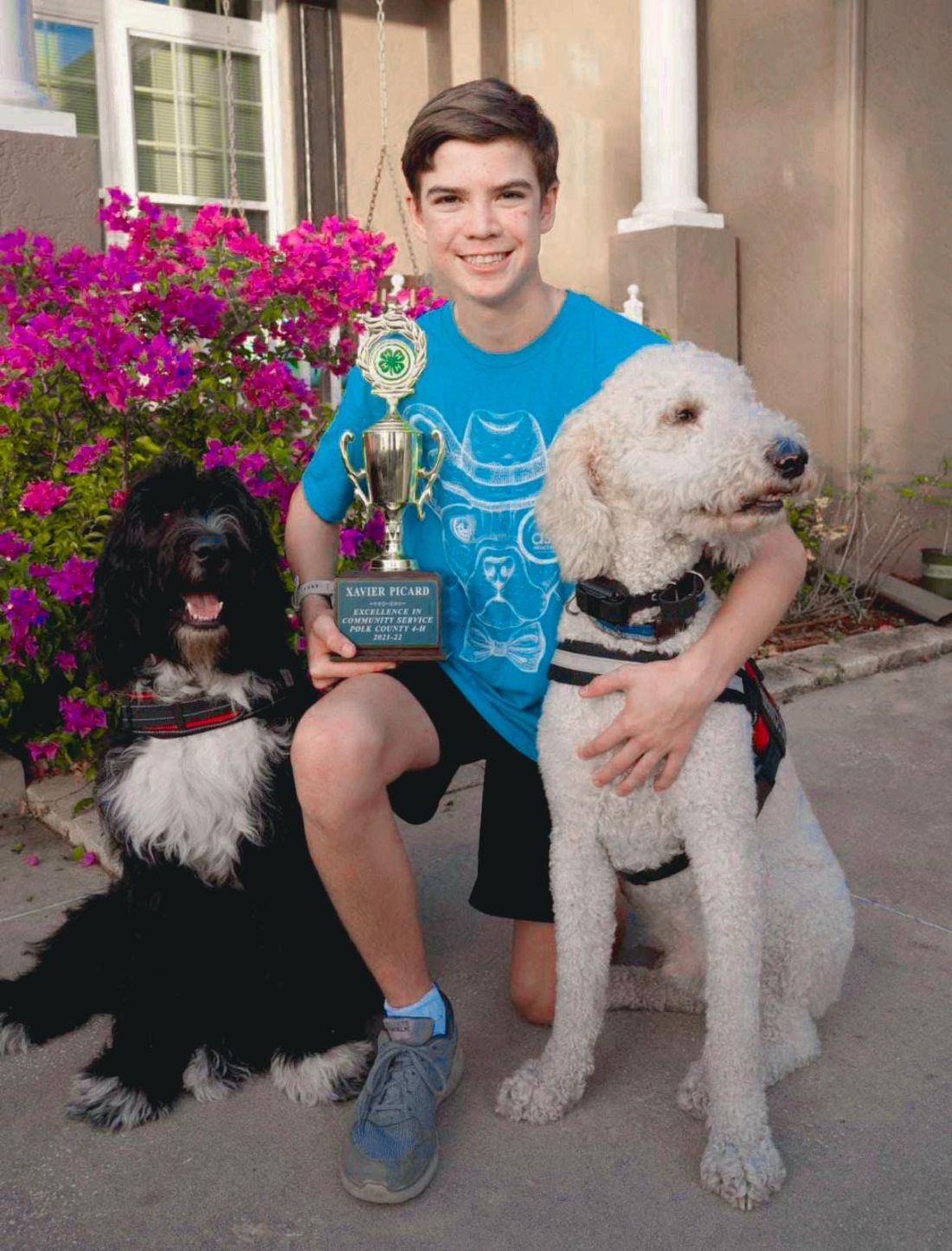 A boy posing holding a trophy and posing with two service dogs