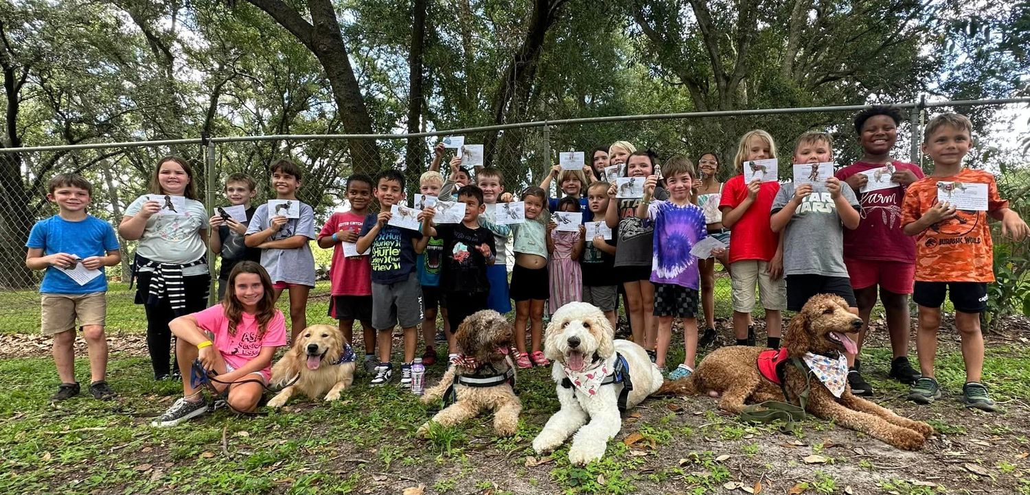 A large group photo of children holding up papers and posing with service dogs in training