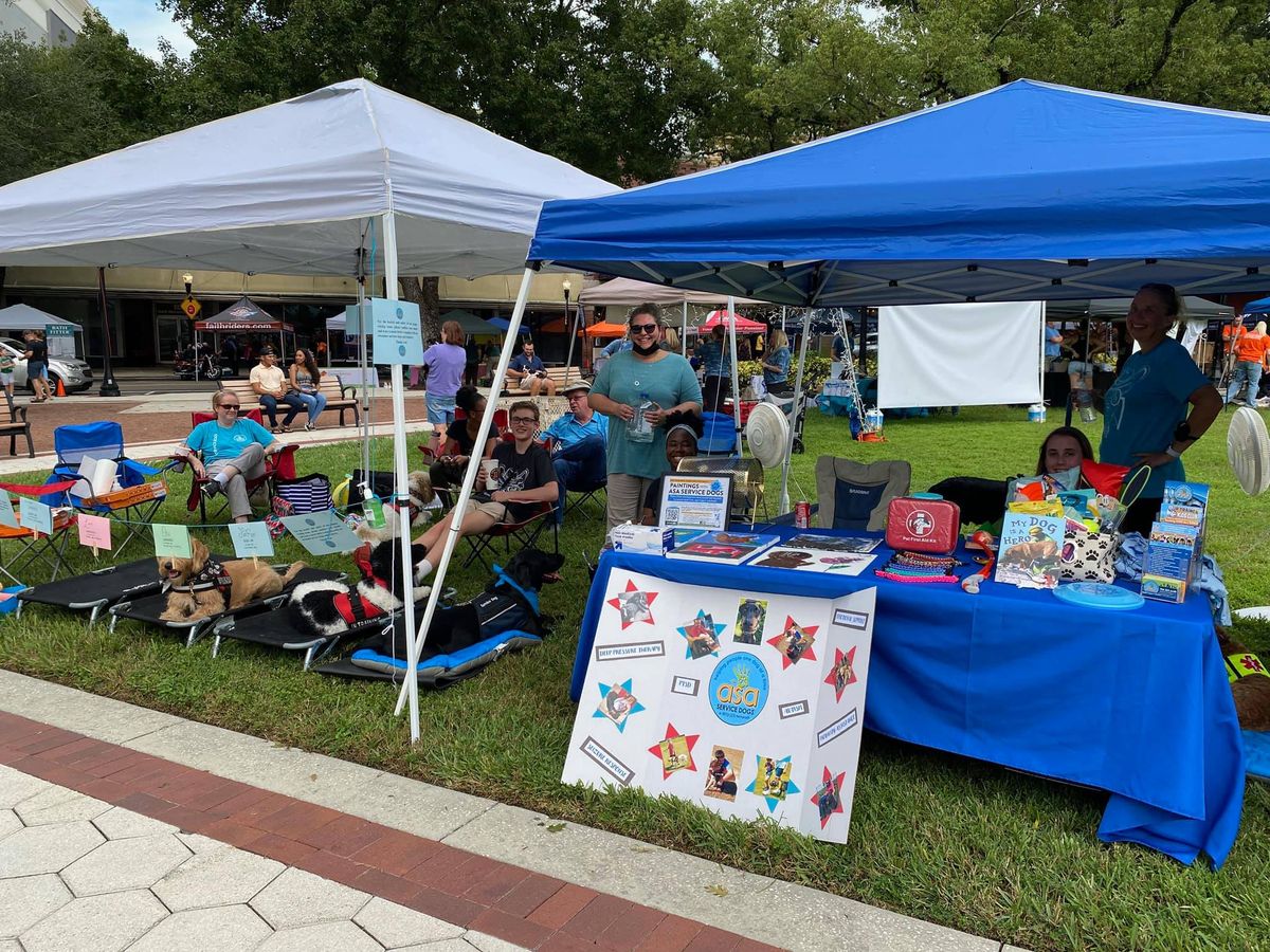 Outside in the grass, one white and one blue pop-up canopy covers ASA Service Dog volunteers
