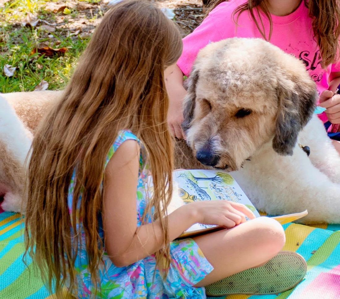 Young girl sits with a service dog in training and reads a story book